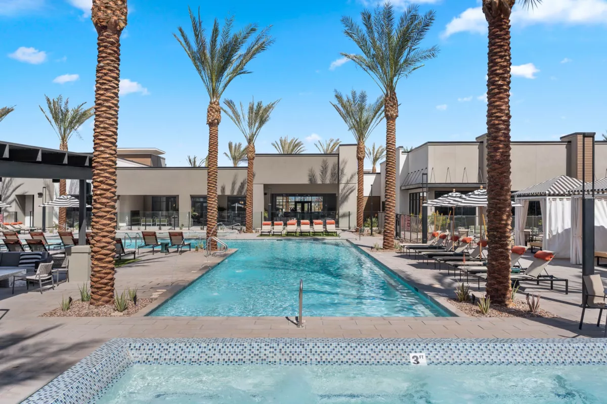 Resort-style pool with palm trees, lounge chairs, striped umbrellas, and water features, surrounded by a modern clubhouse.