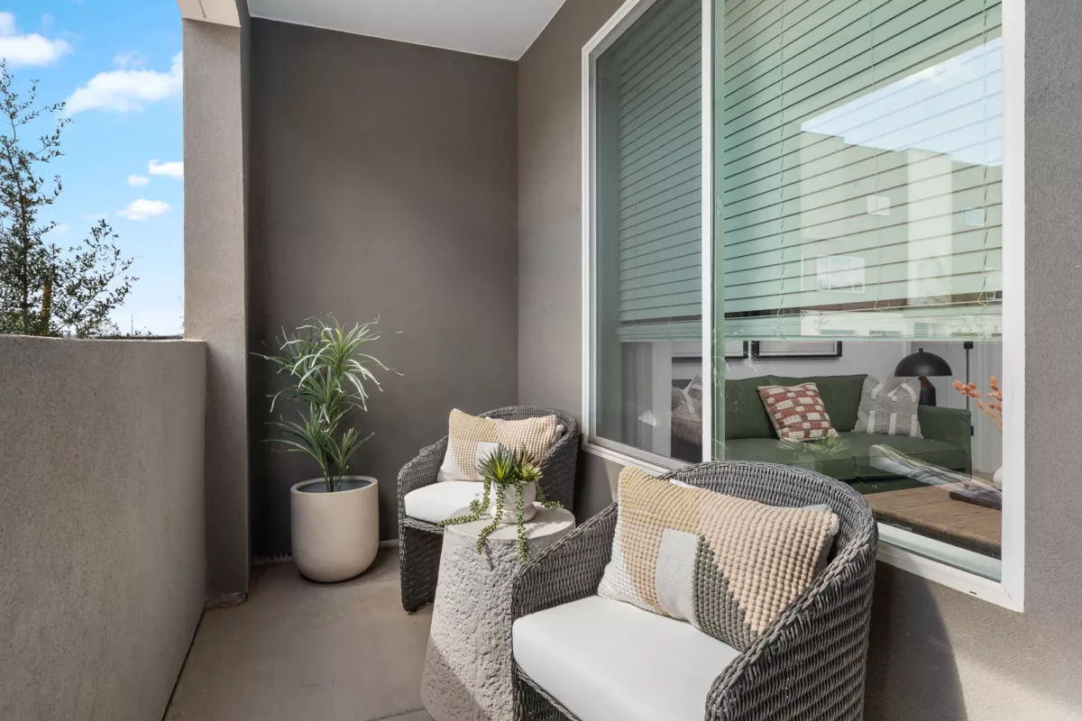 Cozy apartment balcony with two cushioned chairs, a side table, and potted plants.