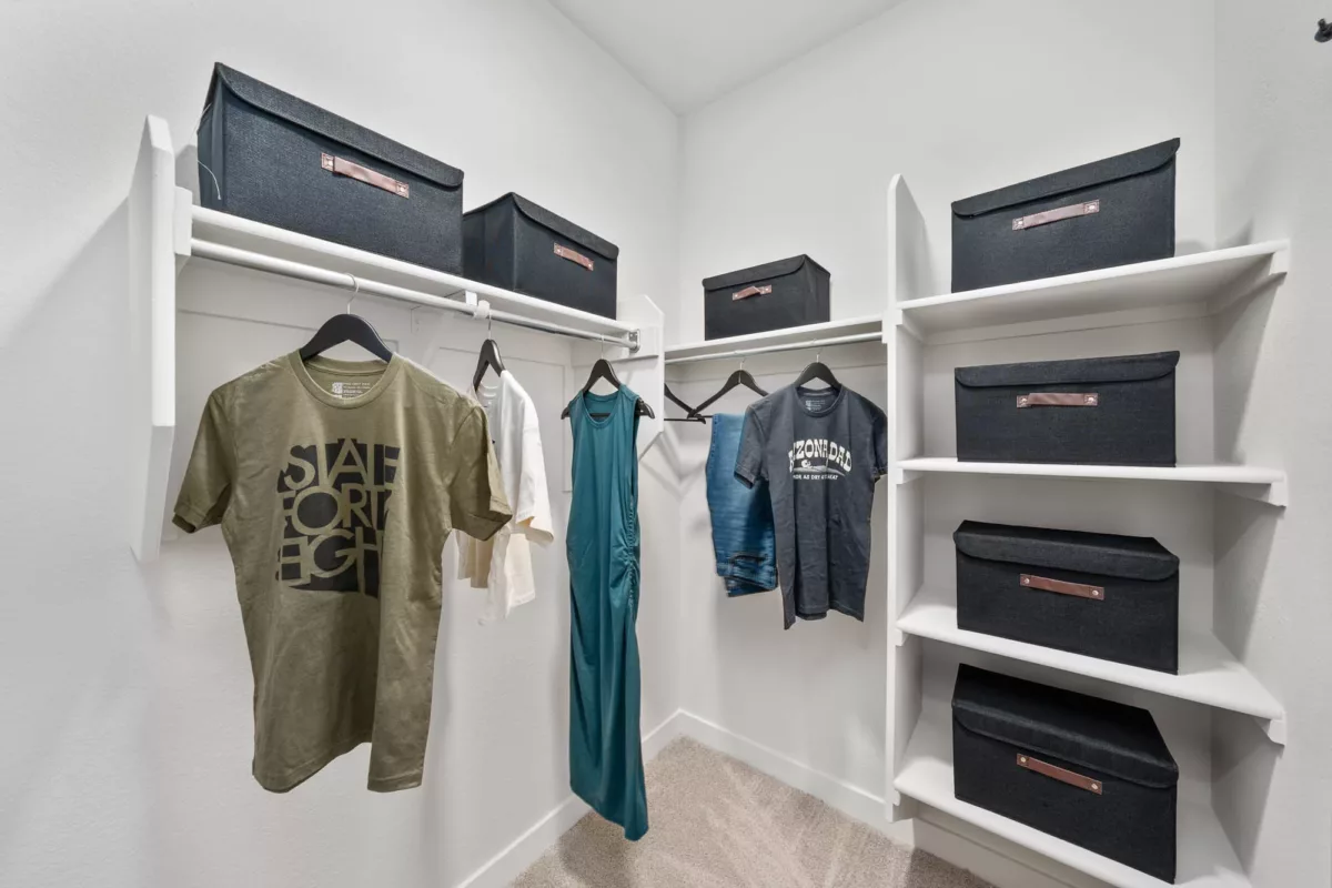 Organized walk-in closet with hanging clothes and labeled black storage bins on shelves.