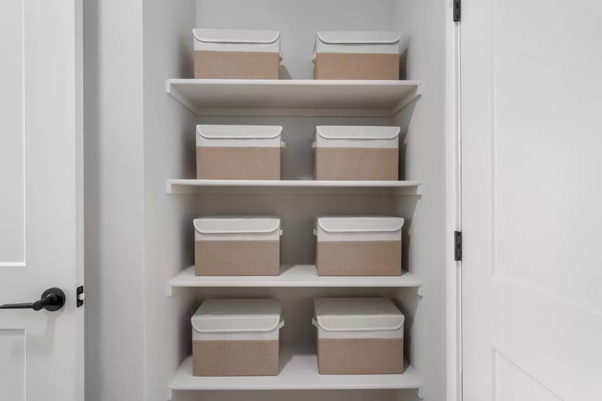 Linen closet with white shelves holding eight beige storage bins with white lids.