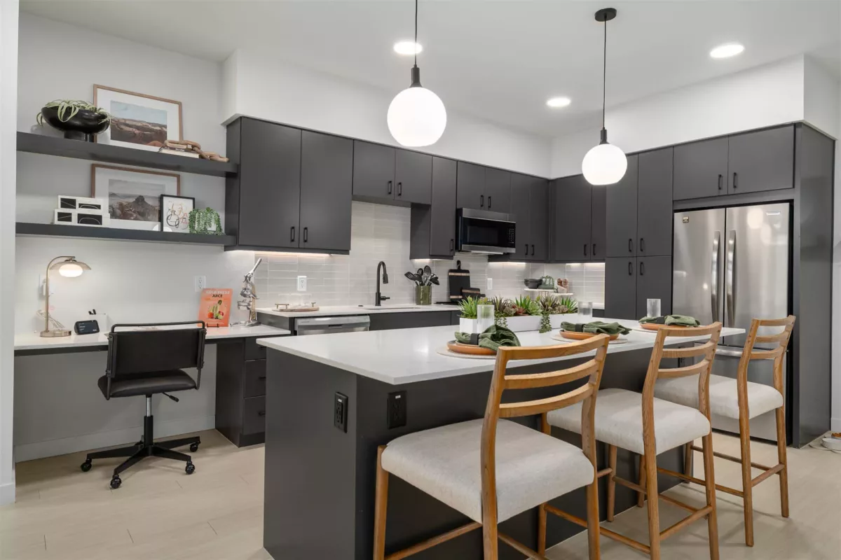 Modern kitchen with black cabinets, white island, barstools, and a built-in desk workspace.