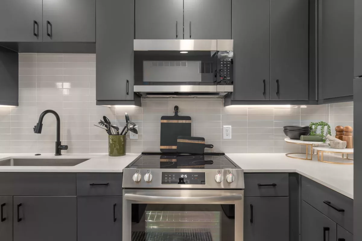 Modern kitchen with black cabinets, stainless steel appliances, a large island, pendant lights over the white countertops, and workstation