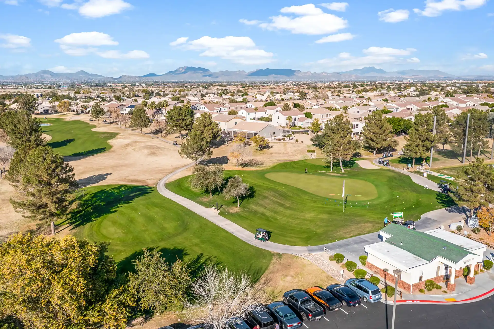 Aerial view of a golf course and a housing development with mountains in the background.