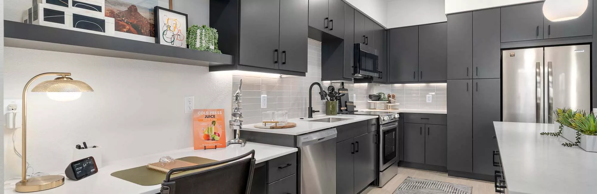 Modern kitchen with built-in desk, black cabinets, stainless appliances, and decorative shelving.