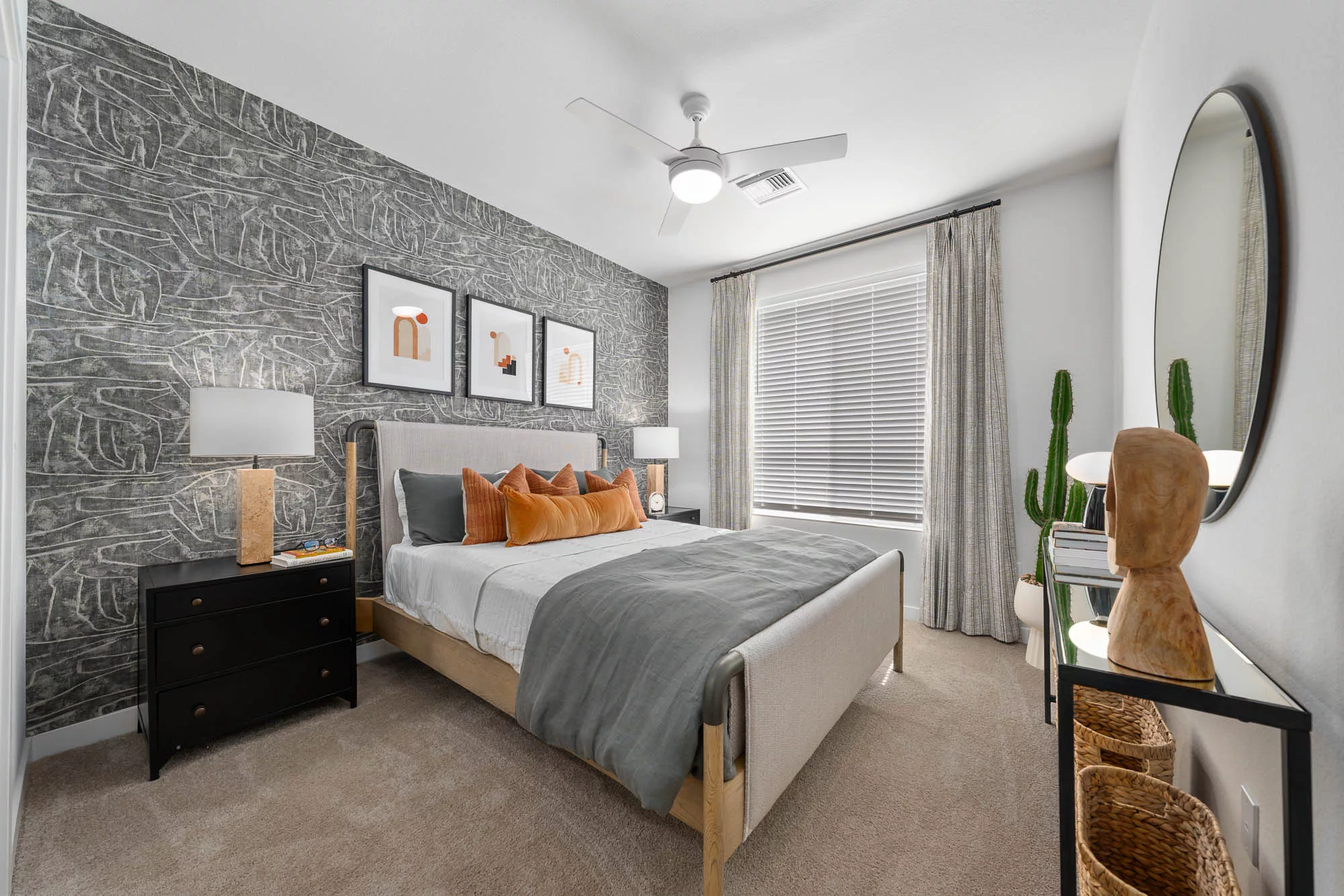 Bedroom with headboard, orange and white bedding, modern artwork, ceiling fan, and large window with blinds.