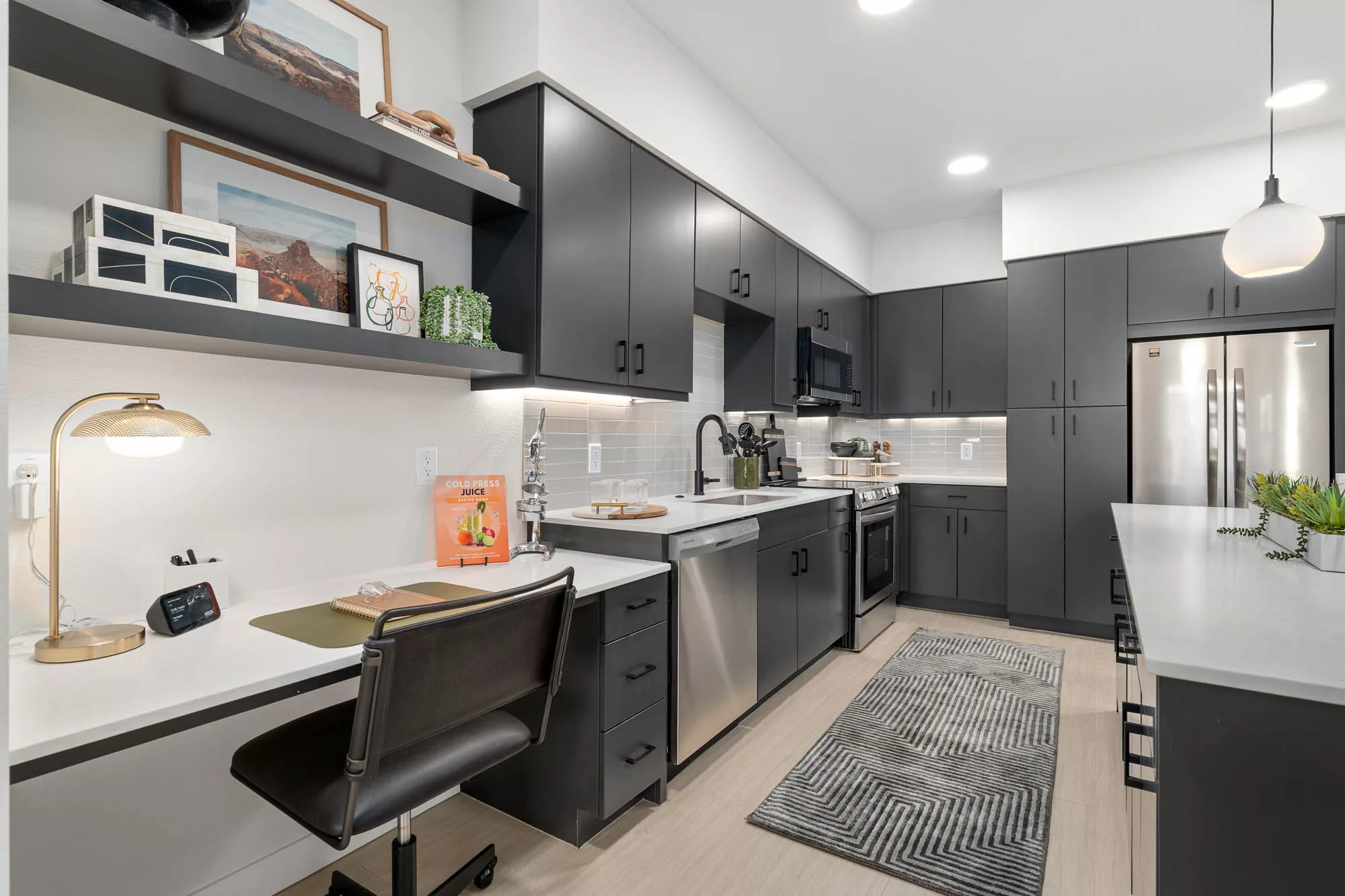 Modern kitchen with black cabinets, stainless steel appliances, undercabinet lighting, grey tile backsplash, and white countertops